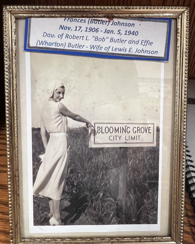 A small gold frame holding a copy of the city-limit photograph, with a typed label above it giving Frances (Butler) Johnson's name, dates and parents
