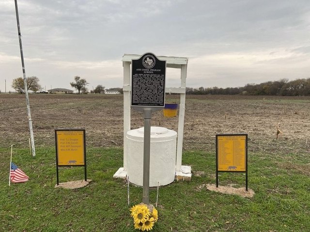 The Ash Creek (Pelham) School site: open ground with the state marker and two yellow signboards