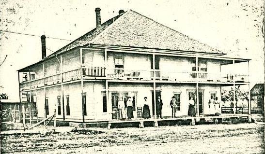 A two-story frame hotel with a deep double porch, people standing along the upper and lower galleries